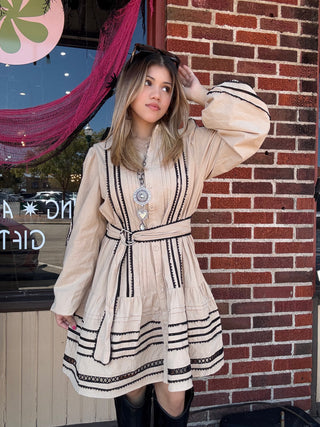 stylish collared neckline, pintuck details, and contrast lace trim on the skirt and belt. The long puff sleeves and smocked back ensure a comfortable, flattering fit