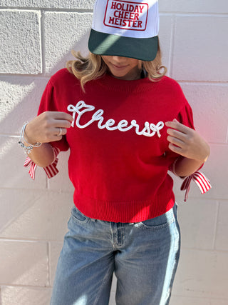 This vibrant red, short-sleeve sweater is the perfect blend of cozy and festive! Knit with a soft, medium-weight yarn, it features a cheerful design meant to spread holiday cheers. A playful, centered decal depicts a classic winter scene, perhaps a steaming mug of cocoa or a smiling gingerbread man, adding a focal point to the piece. Instead of traditional buttons, the neckline is finished with a unique, charming closure: a decorative candy cane bow tie sleeves&nbsp;that drapes sweetly down the front, provi